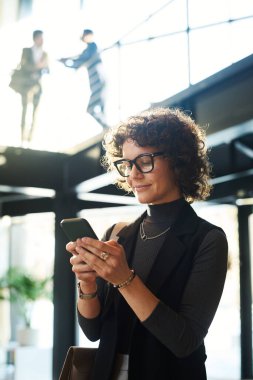 Genç, gülümseyen, gözlüklü bir bayan menajer ve akıllı günlük giyimli iki adamın karşısında dikilirken akıllı telefondan video izliyorlar.