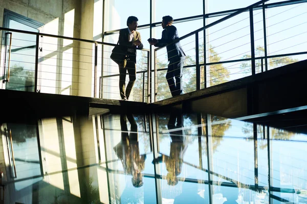 二人の若い男性の同僚の概要オフィスセンターの大きな窓に対して手すりに立って 作業点を議論 — ストック写真