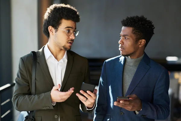 年轻优雅的黑人男子在开会时听到多族裔男同事用智能手机解释某件事情的评论 — 图库照片