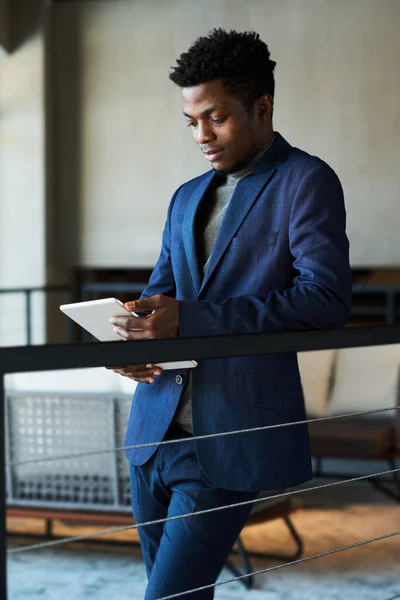 身穿深蓝色西服的年轻而严肃的非洲裔美国商人站在办公大楼走廊里用平板电脑分析网上数据 — 图库照片