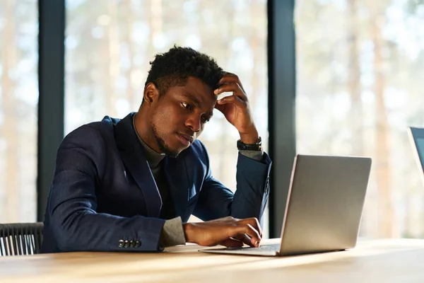 年轻的苦思冥想或紧张的商人坐在办公室的笔记本电脑前 一边看着屏幕上的数据 一边分析数据 — 图库照片