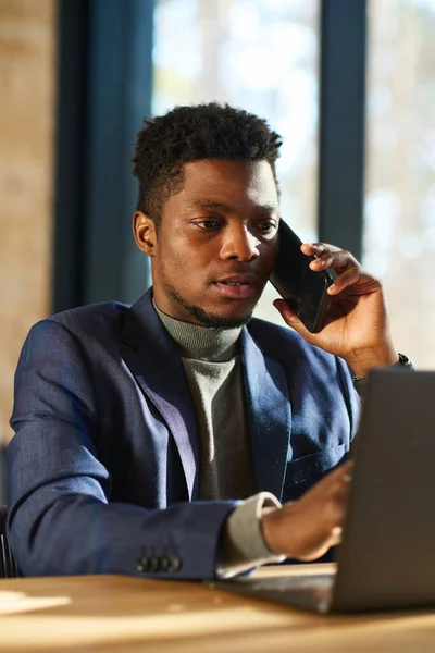 在分析股票市场汇率时 年轻的非洲裔美国男性经纪人用智能手机和笔记本电脑与客户交谈 — 图库照片