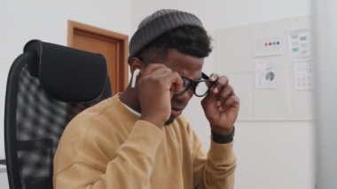 Yavaş çekim, genç Afrikalı Amerikalı programcının gözlüğünü çıkarırken, gözlerini ovuştururken, çay içerken ya da kahve içerken yorulması.