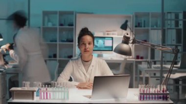 Laboratuar önlüklü, laboratuvar önlüklü, iki kültürler arası meslektaşı kimya laboratuarı boyunca ilerlerken iş yerinin önünde kameraya bakan çok ırklı genç kadın bilim adamının zaman çizelgesi.
