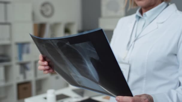 有经验的放射科女医生的特写镜头 她站在医务室的摄像机前 把肺脏的X光影像放在自己面前 并考虑诊断 — 图库视频影像