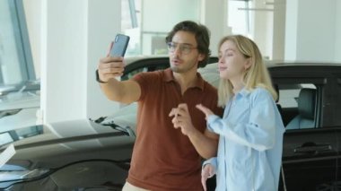 Modern genç çift galeride ellerinde bloglar için yeni bir araba almakla ilgili akıllı telefon kayıt videosu tutuyorlar.