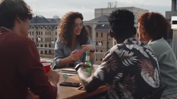 屋上のテーブルに座って乾杯やお酒を飲む多民族の若者のグループ — ストック動画