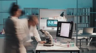 Mikroskop üzerinde çalışırken, bilgisayar kullanırken ve bilimsel deney sırasında laboratuvar boyunca ilerlerken, beyazlar içindeki modern bilim insanlarının birbirleriyle danışma zamanları