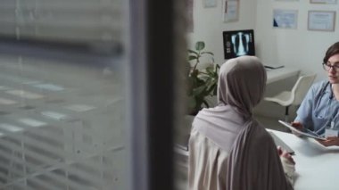 Üniformalı genç radyolog, sunum sırasında önünde oturan ve bazı detayları açıklayan tesettürlü Müslüman kadın hastaya beyin taraması yapıyor.