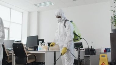 Düşük açılı, tanınmayan uzmanların koruyucu giysiler giyip, kimyasalları dezenfekte ederek ofisi, pandemi konseptini...