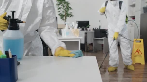 穿着防护服 清扫桌子 在开放式办公室喷洒消毒液的专家的选择性聚焦慢动作 — 图库视频影像