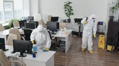 Karantina sırasında modern açık uzay ofisini sterilize eden koruyucu kıyafetler giyen iki dezenfekte uzmanının yüksek açılı görüntüsü.