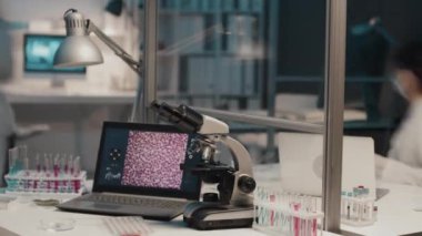 Laptop, mikroskop ve laboratuvar önlüklü ve koruyucu maskeli yoğun bilim adamlarına karşı sıvı maddeli test tüpleriyle modern klinisyenlerin çalışma saatleri.