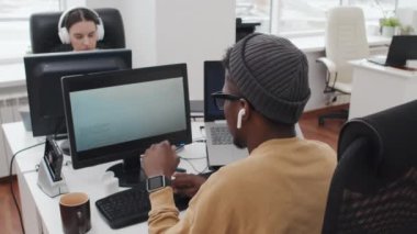 Bilgi işlem şirketinde çalışan genç siyahi bir adamın seçici odak noktası bilgisayardaki verileri saatlerce kodlaması gözlerini ovalamak için küçük bir mola vermesi.