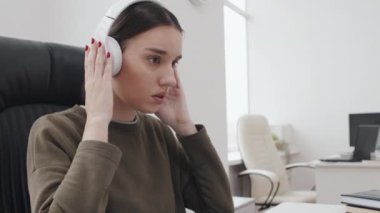 Modern Kafkasyalı, gündelik kıyafetler giyen, bilgisayar başında çalışan ve kulaklıkla müzik dinlemekten hoşlanan genç kadınların orta boy yakın çekimi.