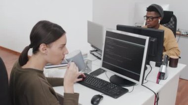 Modern ofiste masa başında oturan, bilgisayar kodları üzerinde çalışan ve çay ya da kahve içen beyaz bir kadının yüksek açılı görüntüsü.