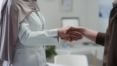Tesettür ve laboratuvar önlüğü giymiş genç kadın klinisyenlerin ve doktorun iş yerinde el sıkışan hastaların iyi tedavi sonuçları için birbirlerini tebrik ederken ve muayenehaneden ayrılırken