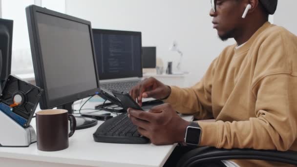 Afrikai Amerikai Programozó Íróasztal Néz Valamit Okostelefonon Megváltoztatja Kódot Laptopon — Stock videók