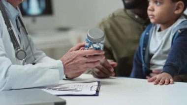 Küçük oğlu olan genç siyahi bir adam klinikte tıbbi danışmanlık sırasında olgun doktorla iletişim kurarken onun tavsiye ettiği bir kavanoz ilacı alıyor.
