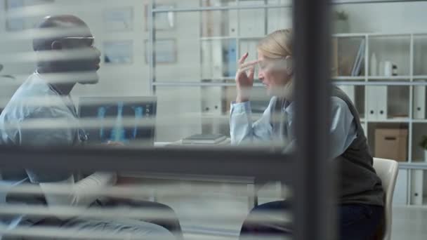 目の前の職場に座り手をカバーしながら 診察中に危険な病気で成長した女性患者を慰める制服と眼鏡の若い医師 — ストック動画