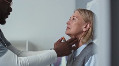 Genç erkek klinisyen elinde özel tıbbi aletle yetişkin kadın hastaların gözlerine ışık tutuyor. Hastanedeki muayene sırasında göz bebeği tepkisini kontrol ediyor.