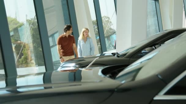 現代の若い夫婦は 彼らの基準や予算に合った車を探してディーラーセンターショールームに沿って歩く — ストック動画