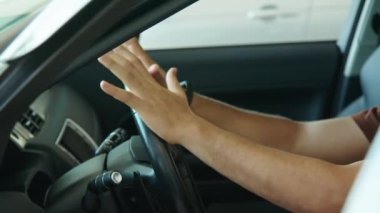 Orta ölçekli, neşeli Orta Doğulu genç bir adam yeni arabasında oturmuş direksiyona dokunuyor.