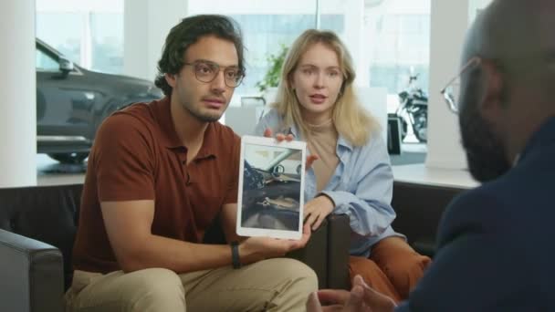 年轻的中东男子和他的白人妻子坐在非洲裔美国人经销商前的扶手椅上讨论汽车内部的特点 — 图库视频影像