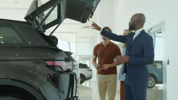 Średni Strzał Afroamerykańskiego Sprzedawcy Pokazujący Jak Zamknąć Bagażnik Nowego Modelu — Wideo stockowe