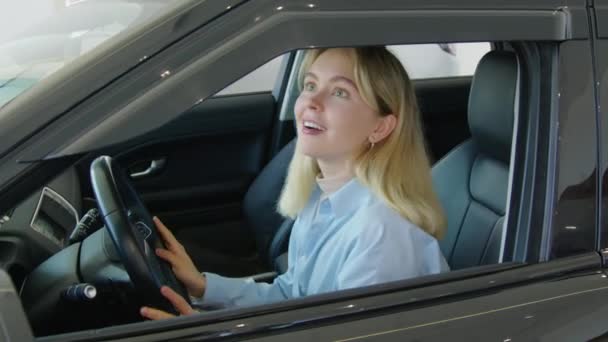 快乐的年轻白人女人坐在横穿马路的车里 在展示室里探索着它的内部 触摸着里面的一切 — 图库视频影像