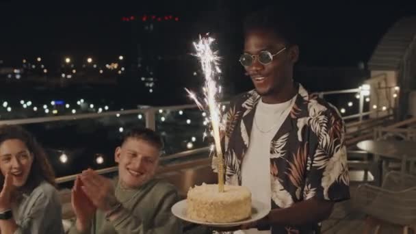 Młody Czarny Mężczyzna Przynosi Tort Urodzinowy Ozdobiony Ogniem Imprezie Dachu — Wideo stockowe