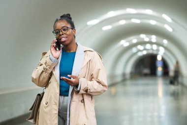 Genç, gülümseyen kız öğrenci ya da çalışan kulak yoluyla metroda dikilirken biriyle iletişim kuruyor.