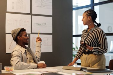 Genç kendine güvenen mimar, yeni binaların çizimleriyle tahtayı işaret ediyor ve sunum sırasında bayan meslektaşına bakıyor.
