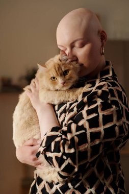 Onkolojik hastalığı olan kel bir kadın, kabarık bir kediye sevgisini ifade ederken, ellerinin arasında tutuyor ve burnunu hayvan başından ayırmıyor.