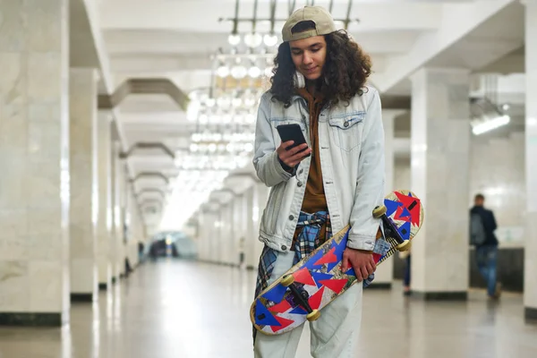 Teenager Mit Skateboard Blickt Auf Smartphone Bildschirm Während Durch Tunnel — Stockfoto
