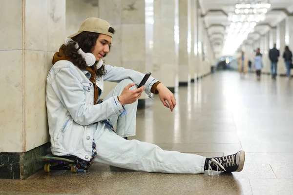 携帯電話のテキストメッセージ オンラインビデオを見たり 地下鉄の駅に座っている間に彼のプレイリストを見ているティーネージャーの側面図 — ストック写真