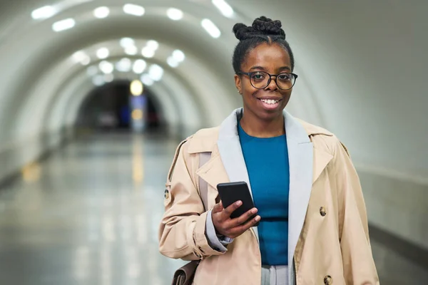 年轻的女商人穿着休闲装 智能手机看着你 站在长长的地铁隧道里的摄像机前 — 图库照片