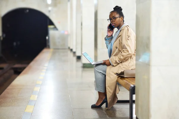 年轻女子坐在地铁站时 手持笔记本电脑和智能手机 一边叫出租车 一边怀疑是否还在等最后一班火车 — 图库照片