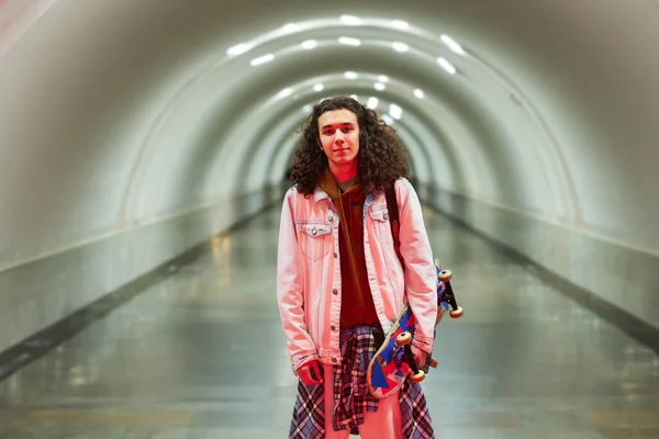 时尚的年轻人 手拿滑板 面对着长长的地铁站或地铁隧道站在镜头前看着你 — 图库照片