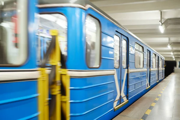 Uzun mavi metro treninin manzarası. İçerideki insanlar yüksek hızda hareket ediyorlar. Boş platform boyunca ve aydınlatılmış metro tüneli boyunca.