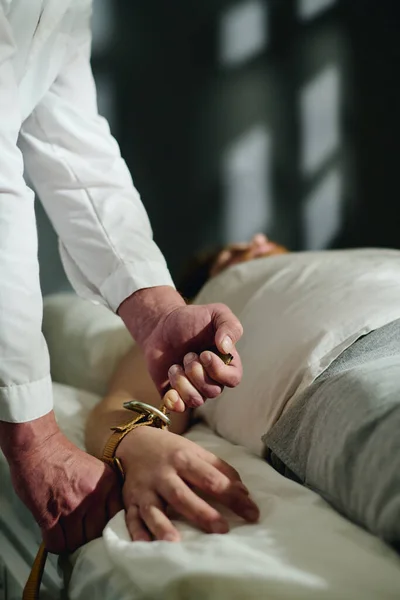 精神病医院医生的手 系紧带男病人的实验室外套 在使他平静下来后弯下腰去 绑住他的手腕 — 图库照片
