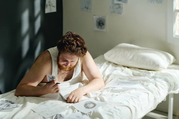 Молодий Чоловік Тривожним Розладом Нахиляється Над Ліжком Малює Фотографії Аркушах — стокове фото