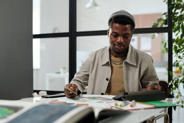 年轻的非裔美国男性建筑师或设计师坐在办公室的工作场所旁边 一边用平板电脑 一边在网上寻找创意 — 图库照片
