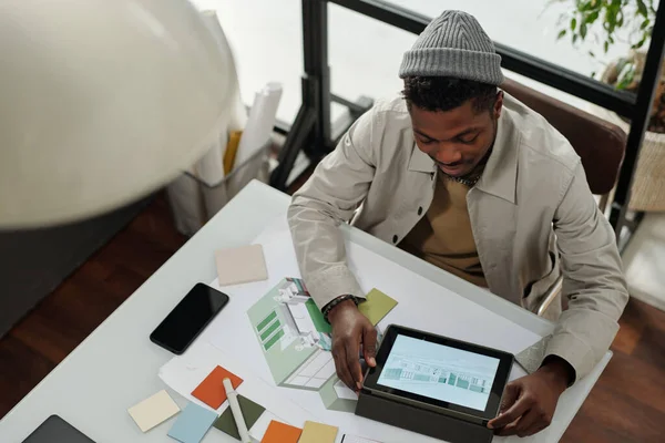 上图是年轻的非洲裔美国人专家坐在桌旁为新项目工作时 使用屏幕上有图形草图的平板电脑 — 图库照片