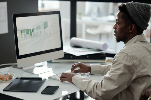 身穿便服的年轻黑人男子一边在电脑屏幕上看草图 一边为新的建筑项目绘图 — 图库照片