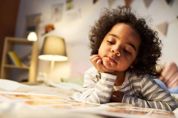 Aranyos Afro Amerikai Kisfiú Néz Képeket Könyvben Miközben Fekszik Ágyban — Stock Fotó