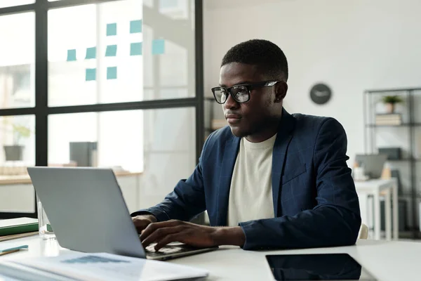 Νεαρός Σοβαρός Αφροαμερικανός Επιχειρηματίας Δακτυλογραφεί Στο Πληκτρολόγιο Laptop Ενώ Κάθεται — Φωτογραφία Αρχείου