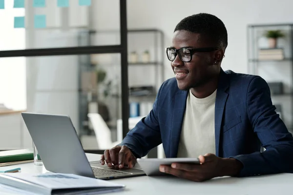 Jovem Empresário Sorridente Óculos Olhando Para Tela Laptop Enquanto Analisa — Fotografia de Stock