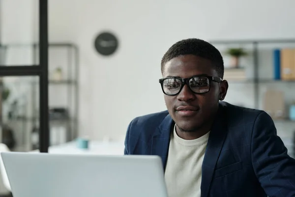 Młody Poważny Pracownik Biały Kołnierz Okularach Siedzi Przed Laptopem Patrzy — Zdjęcie stockowe