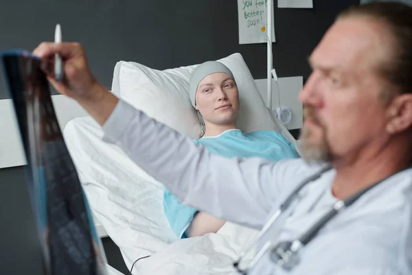 年轻的脑癌妇女躺在床上 看着肿瘤专家分析X光图像 并对医院病房的Mri扫描结果进行分析 — 图库照片